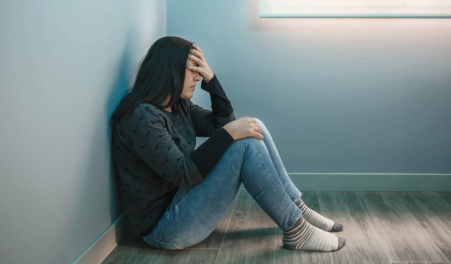 Lonely sad woman deep in thoughts sitting daydreaming or waiting for someone in the living room with a serious expression, she is pensive and suffering from depression sitting on wooden floor.