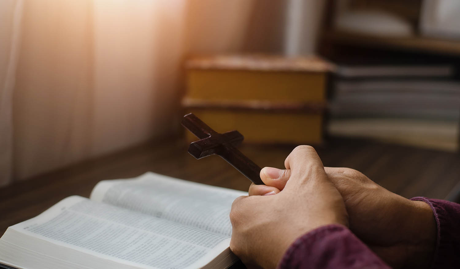 Hand holding religious crucifix cross on top of Holy Bible. Christian faith and devotion concept.