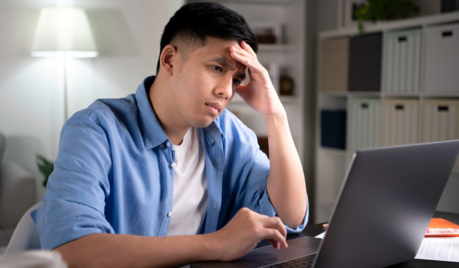 Unhappy young Asian man, entrepreneur, student, tutor looking at laptop screen with serious and worried face and with hand on forehead when working or learning from home.