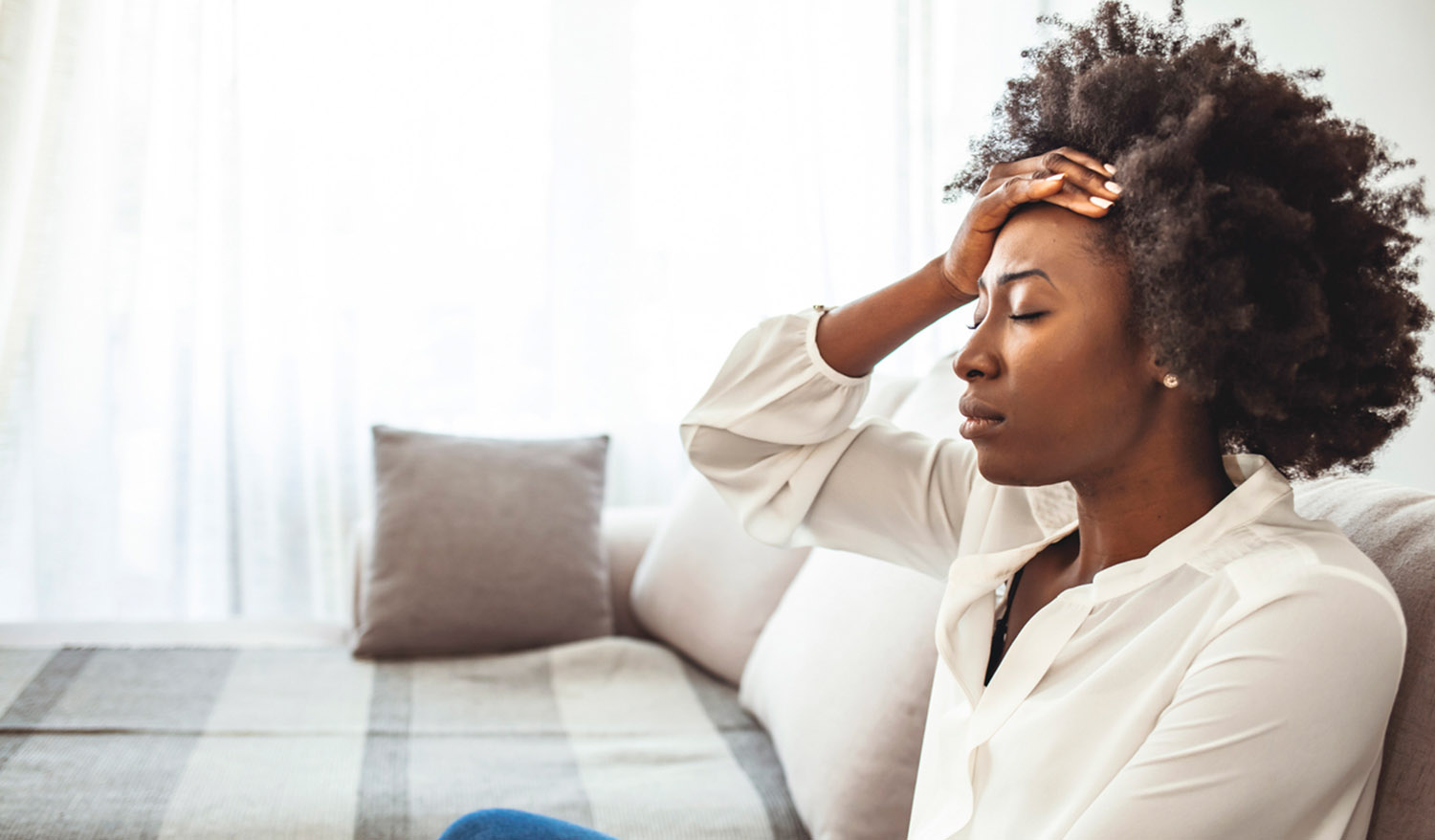 Lonely sad woman deep in thoughts sitting daydreaming or waiting for someone in the living room with a serious expression, she is pensive and suffering from insomnia sitting on couch